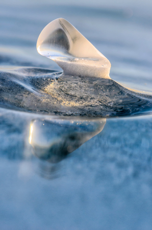 Ice floe at frozen lake surface with reflection. Deep cracks in the ice and ice reflectionの写真素材