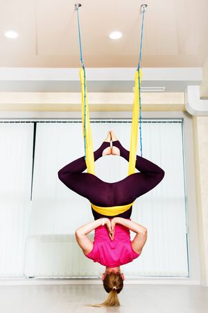 Fit pretty young woman wearing sportwear doing fly yoga stretching exercises in fitness training white gym loft classroom.の写真素材