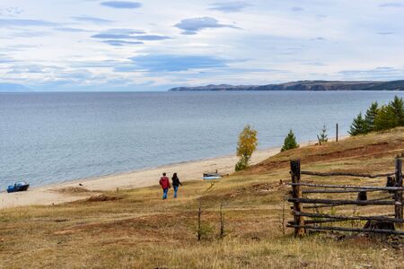 Two people silhouettes walk in the seasid of Lake Baikal, tree and mountains of Siberia with beautiful sky and clouds, Russia Oklhon islandの写真素材