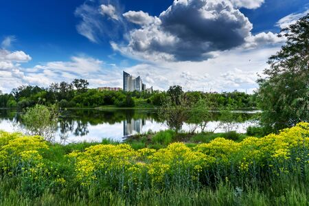 Modern building is reflected in lake in city Park. Summer Sunny day in a city with beautiful cloudsの写真素材