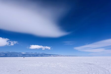 Silhouette of man rides bicycle on the frozen lake Baikal in sunny weather with beautiful clouds skyの写真素材