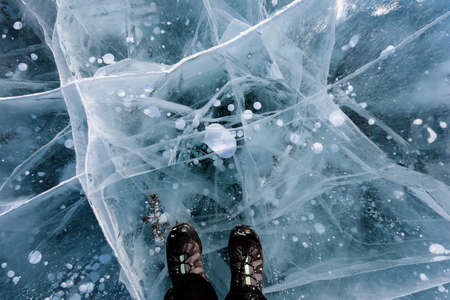 Beautiful ice of Lake Baikal with abstract cracks with shoes. Top view