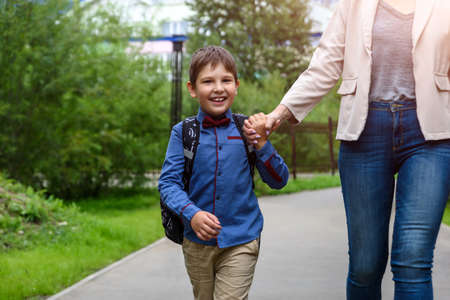 Parent and pupil of primary school go hand in hand. Woman and boy with backpack behind the back.の写真素材