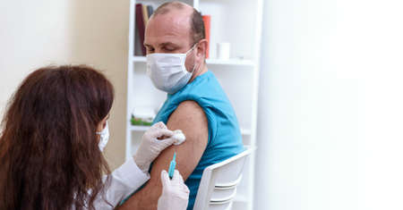 Doctor in gloves holding syringe and making injection to patient in medical mask.の写真素材