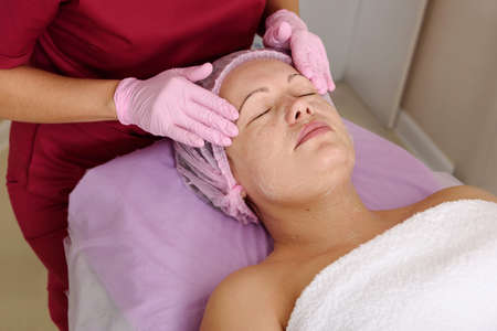 Face peeling mask, spa beauty treatment, skincare. Woman getting facial care by beautician at spa salonの写真素材