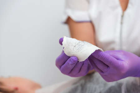 Hand with purple gloves are holding used wax stripes with removed hair. Depilation skin in spa salonの写真素材