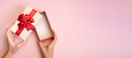 Hands holding open gift box with red bow on pink background. Top viewの写真素材