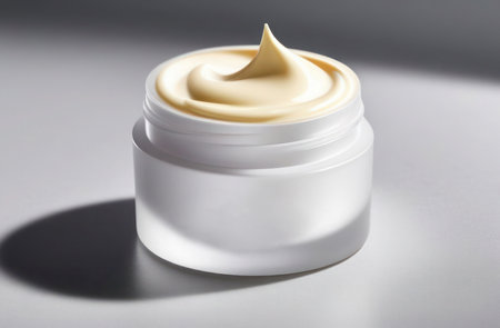 Glass jar of beauty cream resting on side and reflected in white surface.の素材