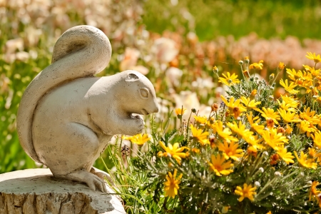 A Cute Stone Chipmunk Statue Made of Stone in a Yard Setting With Flowersの写真素材