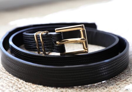 black leather belt with golden buckle on a gray textured backgroundの写真素材