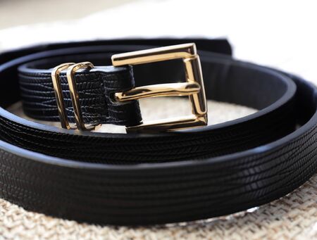 black leather belt with golden buckle on a beige textured backgroundの写真素材