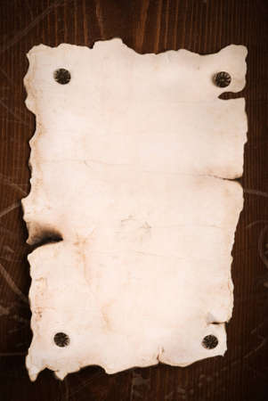old paper with burnt torn edges on wooden wall, focus point on centerの写真素材