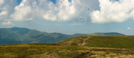 Competitions of paragliders on the ridge of Borzhava in the Carpathians in Ukraine. Panoramic photo of a large group of paragliders in the sky above the mountains.の写真素材