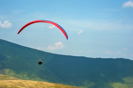A paraglider flies over a mountain valley on a sunny summer day. Paragliding in the Carpathians in the summer.の写真素材