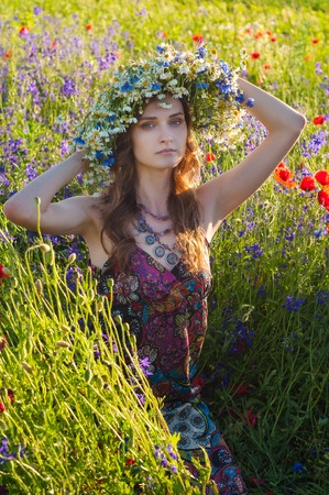 Girl with a wreath of flowers. Face of beautiful ukrainian girl in a wreath of summer flowers on nature. Girl on the field with poppies. Fantasy art photography.の写真素材