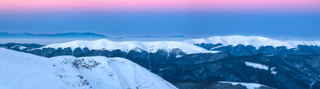 Wonderful pink sunrise in the Carpathians in the winter. Panoramic photo of snow-covered summits of winter mountains in the rays of sunrise. Snow-capped mountain top like ice cream.の写真素材