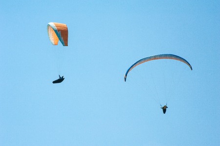 Two paragliders flying on the background of blue sky. Paragliding in the sky on a sunny day.
