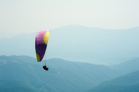 Paraglider flies over a mountain valley on a sunny summer day. Paragliding in the Carpathians in the summer.の写真素材