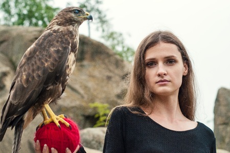 Beautiful girl holding a falcon in her arms. Brunette among the rocks holding a wild bird on a ball...
