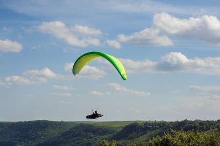 Paragliding over the green field in summer sunny day. One paraglider fly over a green field near Dnister river in Ukraine.のeditorial素材