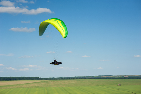Paragliding over the green field in summer sunny day. One paraglider fly over a green field near...