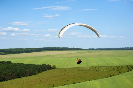 Paragliding over the green field in summer sunny day. One paraglider fly over a green field near Dnister river in Ukraine.のeditorial素材