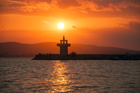 Lighthouse against a beautiful evening sunset on the sea. Amazing sunset on black sea and beautiful cloudscape.の写真素材