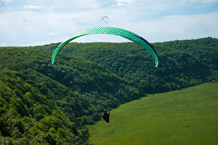 Paragliding over the green field in summer sunny day. One paraglider fly over a green field near Dnister river in Ukraine.の写真素材