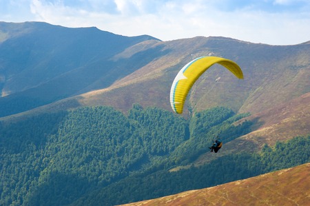 Paraglider fly over a mountain valley on a sunny summer day. Paragliding in the Carpathians in the...