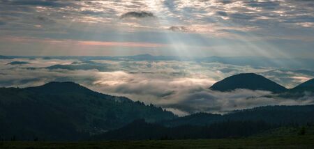 Amazing sunrise in the mountains. Great view of the foggy valley with bright sun rays in Carpathians. Impressive mountain landscape with rising sun and rugged mountains raise above the clouds.の写真素材