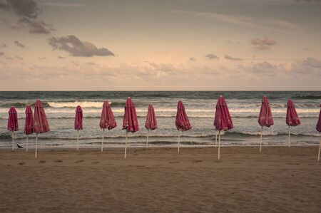 Closed beach umbrellas on the beach at sunset. Sea with waves and sky with clouds on the background. September 13, 2018, photo of the beach at the hotel, Sozopol, Bulgaria.のeditorial素材