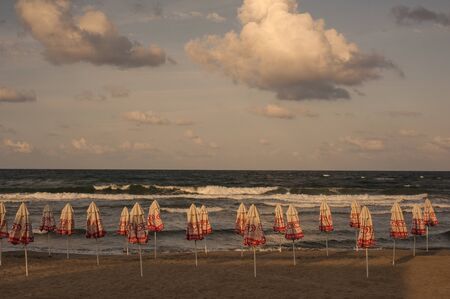 Closed beach umbrellas on the beach at sunset. Sea with waves and sky with clouds on the background. September 13, 2018, photo of the beach at the hotel, Sozopol, Bulgaria.のeditorial素材