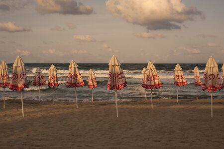 Closed beach umbrellas on the beach at sunset. Sea with waves and sky with clouds on the background. September 13, 2018, photo of the beach at the hotel, Sozopol, Bulgaria.のeditorial素材