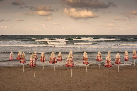 Closed beach umbrellas on the beach at sunset. Sea with waves and sky with clouds on the background. September 13, 2018, photo of the beach at the hotel, Sozopol, Bulgaria.のeditorial素材