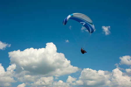 Blue paraglider flying in the blue sky against the background of clouds. Paragliding in the sky on a sunny day.の写真素材