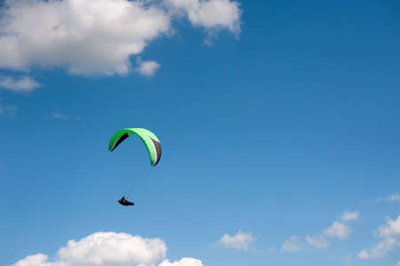 Alone green paraglider flying in the blue sky against the background of clouds. Paragliding in the sky on a sunny day.の写真素材