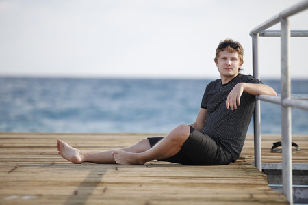 A man sits on the dock at waterの写真素材