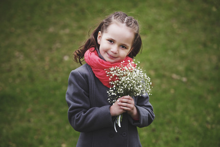 Baby girl with a bouquet of white flowers on a background of grassの写真素材