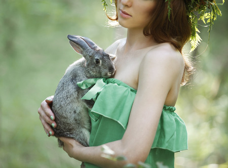 Beautiful model with a gray rabbit in her arms in green summer forestの写真素材