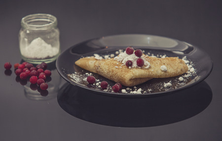 The pancakes are served on a black plate on a black background with reflectionの写真素材