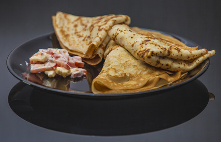 The pancakes are served on a black plate on a black background with reflection