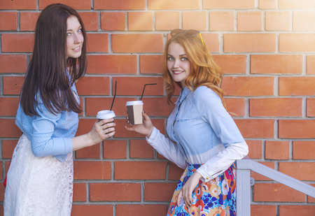 Two girls with cups of coffee talk on the background wallの写真素材