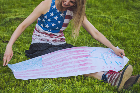 Female model against a green lawn in a t-shirt with the American flagの写真素材