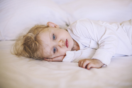 European small child lying on the bed. White, sad, beautiful, boy, girlの写真素材
