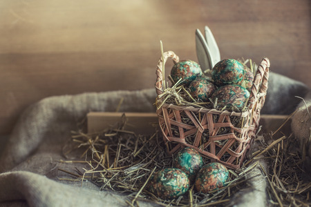 Easter eggs on rustic background with straw, textiles and baskets and hidden Bunny earsの写真素材