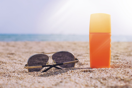 Sunglasses and sun cream in the sand against the sea in the rays of sunlight and glareの写真素材