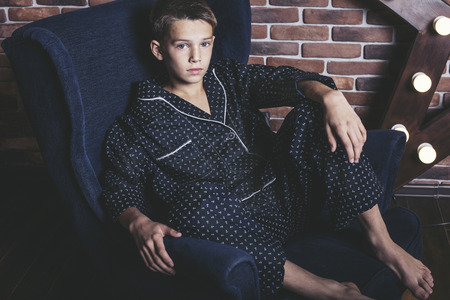Beautiful trendy teen boy sitting on a chair at home in your pajamasの写真素材