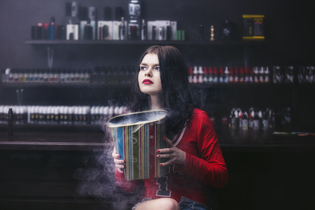Young beautiful brunette woman with fashion makeup at the bar with a with vapor from electronic cigaretteの写真素材