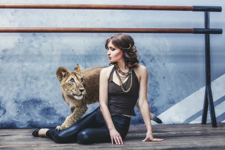 Beautiful fashionable young woman with a cute little alive lion cubの写真素材