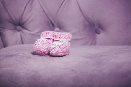 Pink knit little baby booties closeup standing on the couchの写真素材
